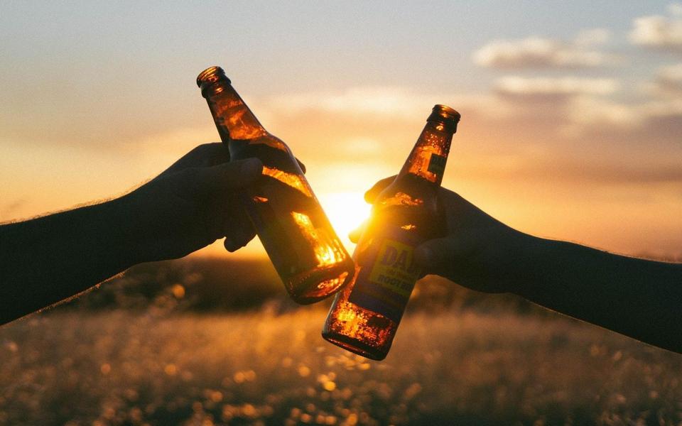 黃昏的陽光下，兩只手拿啤酒瓶干杯慶祝的桌面壁紙圖片