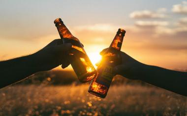 黄昏的阳光下，两只手拿啤酒瓶干杯庆祝的桌面壁纸图片